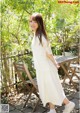 A woman in a white dress standing next to a wooden table.