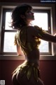 A woman in a gold outfit standing by a window.