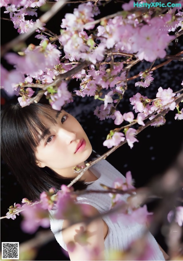 A woman standing in front of a tree with pink flowers.