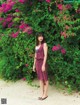 A woman standing in front of a bush of pink flowers.