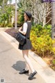 A woman walking down a sidewalk carrying a black bag.