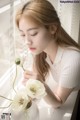 A woman sitting at a window sill with a vase of flowers.