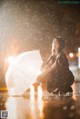 A woman crouching down in the rain holding an umbrella.