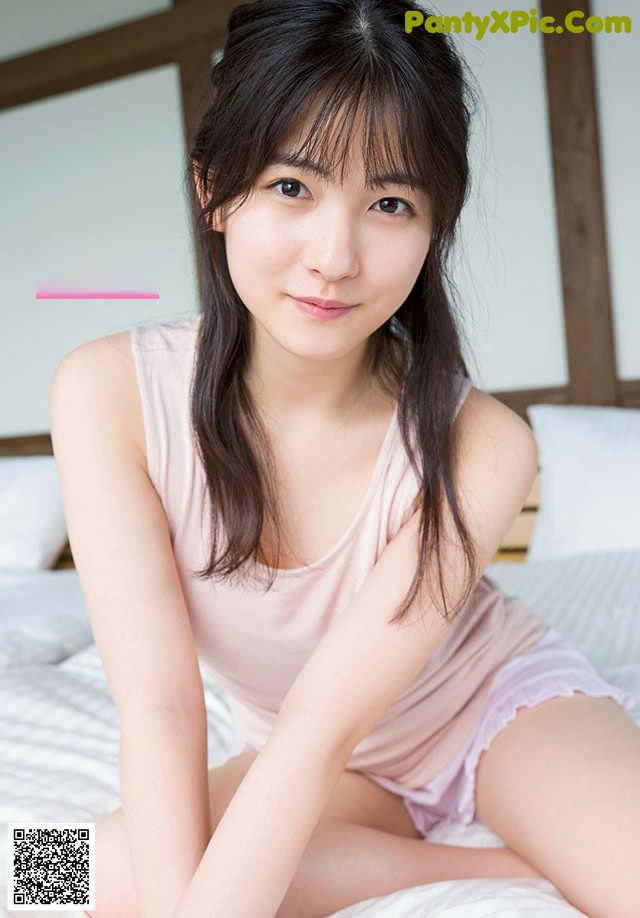 A woman sitting on top of a bed in a pink shirt.