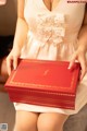 A woman in a white dress holding a red box.